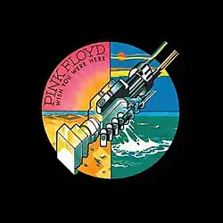 The black plastic covers the whole vinyl package. The circle sticker at the right-centre position shows two machines clasped together, resembling a handshake. The whole circle is divided into four quarters in different colours. The pink quarter, located on upper-left, has the sun shining and "PINK FLOYD" in big font; below the band name is "WISH YOU WERE HERE" in small font. The yellow quarter is at lower-left displaying sand dunes. The blue quarter is at upper-right showing blue skies. The green quarter is at south displaying green-coloured water.