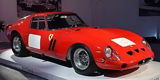 A bright red racing car with blank, square white numbmer patches, on a white showroom platform