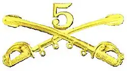 A computer generated reproduction of the insignia of the Union Army 5th Regiment cavalry. The insignia is displayed in gold and consists of two sheafed swords crossing over each other at a 45 degree angle pointing upwards with a Roman numeral