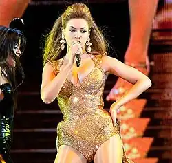 Beyoncé stands looking out to a crowd while holding a microphone