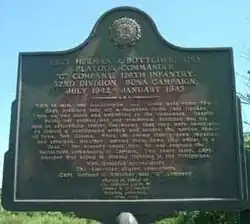 The memorial plaque at the entrance to Buna Village, dedicated to Herman Bottcher and the 32nd Red Arrow Division Infantry Division.