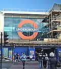 A building with scaffolding around it and a large window with a sign reading "UNDERGROUND" in white letters on a blue rectangle