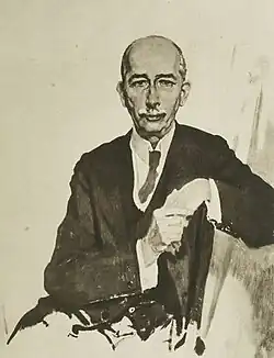 Frontal image of House with white mustache; seated with hands folded in his lap.
