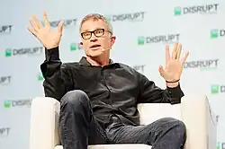 A picture of David Baszucki speaking while sitting in a chair