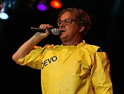 Mothersbaugh holding a microphone to his mouth, wearing a bright yellow costume