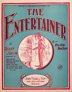 The front cover of The Entertainer sheet music. It has a green background and in the centre is a red ink drawing of a stereotyped African-American performer on stage in top hat and tails