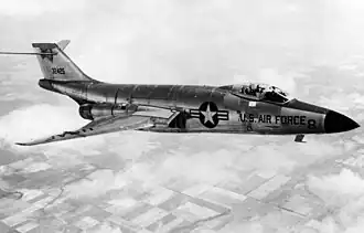 Black-and-white photo of jet aircraft flying right above clouds. On the aircraft's side is a symbol with a star, to the right of which says, U.S. Air Force. Its horizontal stabilizers are located atop its fin.