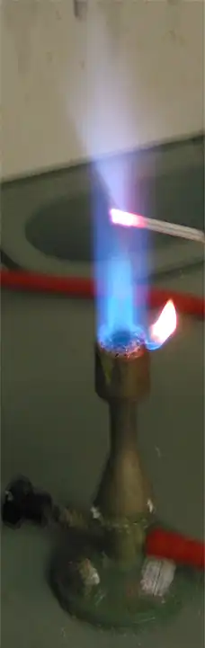 شعله‌ای که یک میله فلزی کوچک در آن نفوذ کرده است؛ شعله در نزدیکی میله آبی کمرنگ است.