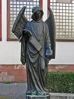 a dark-coloured metal staue of an angel with a broken neck and broken wing