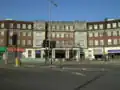 A brown-bricked building with white columns and a sign reading "HENDON CENTRAL STATION" in blue letters all under a clear, blue sky