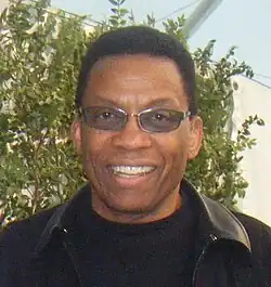 An African American male in his late sixties is wearing sunglasses, a black jacket, and a black T-shirt.
