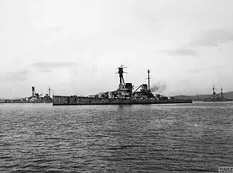 Several large gray warships sit motionless in harbor