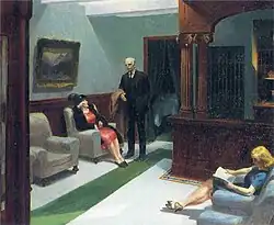 A man and two women sit in a hotel lobby with stark lighting and subdued tones