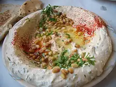یک بشقاب حمص، تزئین شده با پاپریکا و روغن زیتون و آجیل کاج