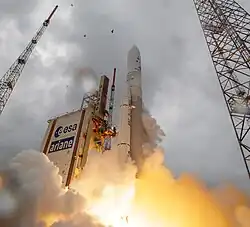 Low-angle shot of a light-colored rocket blasting up towards a gray sky