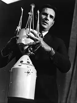 A black and white photograph of a suited man demonstrating two model components interlocking