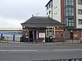 A red-bricked building with a rectangular, dark blue sign reading "KENTON STATION" in white letters all under a blue sky with white clouds