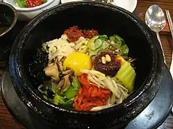 سینی غذای Bibimbap که از گوشت گوساله ، برنج و سبزیجات پخته تشکیل شده که با روغن و سس سویا ترکیب و در یک کاسه سنگی پخته می‌شود