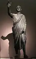 متصدی ، ۱۰۰ سال قبل از میلاد ، مجسمه برنزی ایتروسکو-رومی که آول متل را به تصویر می‌کشد (لاتین: Aulus Metellus) ، مردی اتروسیایی که در حالی که مشغول بلاغت بود ، یک توگا رومی پوشید . این مجسمه دارای کتیبه ای به الفبای اتروسک است