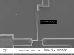 A photomicrograph of a vibrating cantilever.  Cursors on the picture indicate that the peak-to-peak amplitude of the vibration is 17.57μm.