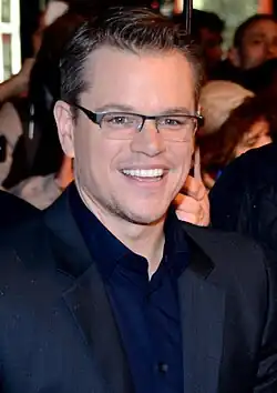 A man is wearing a navy blue collared shirt and glasses.