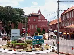 Town scene with three-storied red houses and a red church. There is a three-storied clock tower standing on a square.