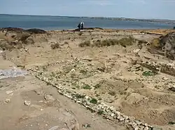 The remains of the wall of a small structure are seen in the foreground, the Sea of Azov is visible in the background.