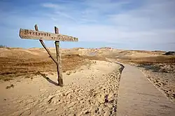 تپه شنی، یک مسیر چوبی و یک تابلو چوبی.