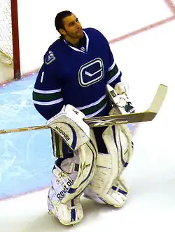 An ice hockey goaltender with his mask pulled off of his face looking forwards. He wears a green jersey with a logo of a stylized orca in the shape of a "C".