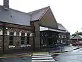A brown-bricked building with a rectangular, dark blue sign reading "RUISLIP STATION" in white letters all under a clear, white sky