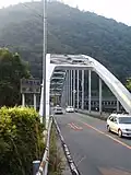پل ساگامی کو اُوباشی (相模湖大橋). راه ورودی کوه ساگامی آراشی در طرف چپ خیابان انتهایی این پل و مخالف جهت بهمن‌گیر قرار دارد.