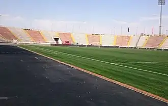 A photo taken close to the touchline showing part of the grass field and the stadium seating surrounding it