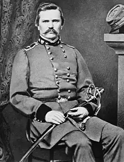 Black-and-white photo of a mustachioed military officer sitting with a saber across his lap