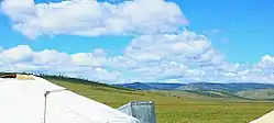 Puffy white clouds roll over lush green hills.