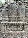  Three stone pillars, aged and a few feet tall sit atop intricate stone carved foundation depicting a face in the center and two flowers on either side