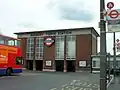 A red-bricked building with a rectangular, grey sign reading "SUDBURY TOWN STATION" in black letters all under a blue sky
