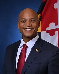 Official gubernatorial portrait of Moore smiling in front of the Maryland flag, wearing a black suit with Maryland flag lapel pin, light blue shirt, and red tie.