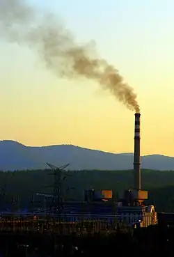Smoke rising from a tall chimney just after sunset against a background of mountains