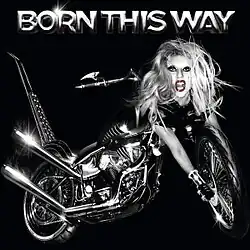 Grayscale image of a bike against a black background. The bike has a blond woman's head at its front, whose right hand stretches out to the front tires of the bike. The words "Born This Way" is embossed above the image.