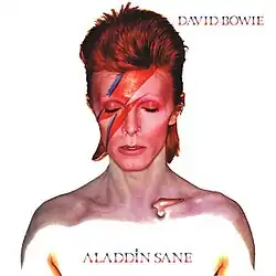A close-up of a white shirtless man with bright red hair with a blue and red lightning bolt across his face