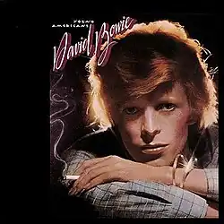 A headshot of an orange-haired man holding a cigarette with a backdrop of light.