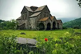 Ancient stone church with many gables sits in a grassy area that is surround by vegetation.