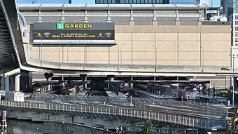 A railway station with five island platforms next to a large arena. Several passenger trains are at the platforms.